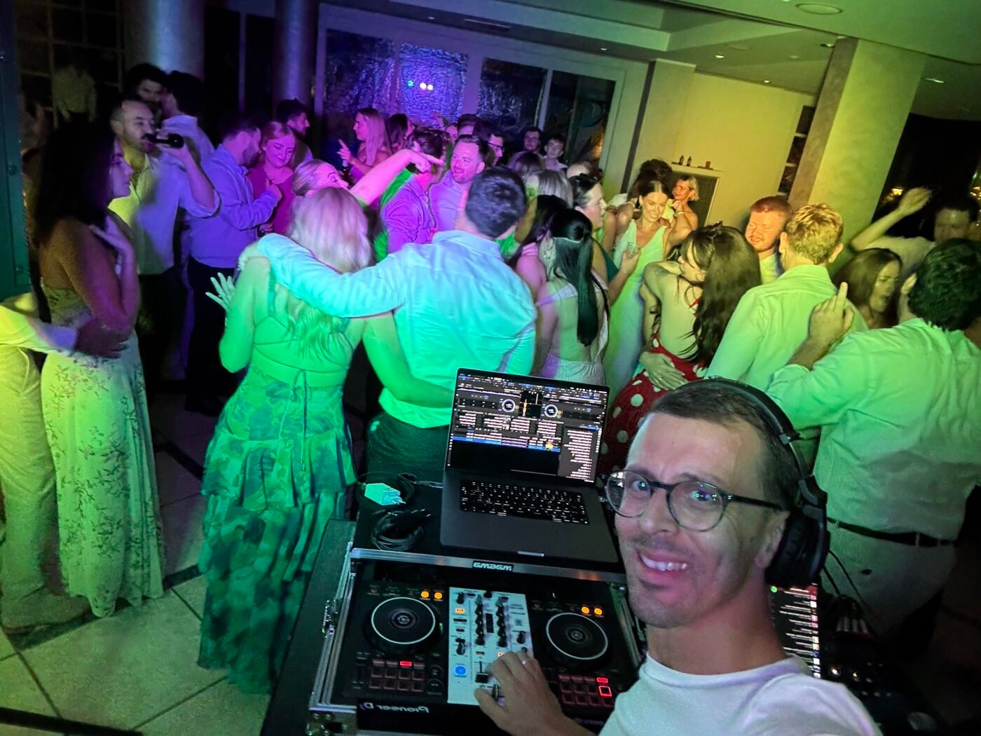 MACO DJ in consolle con le cuffie durante un matrimonio, con gli invitati che ballano in pista
